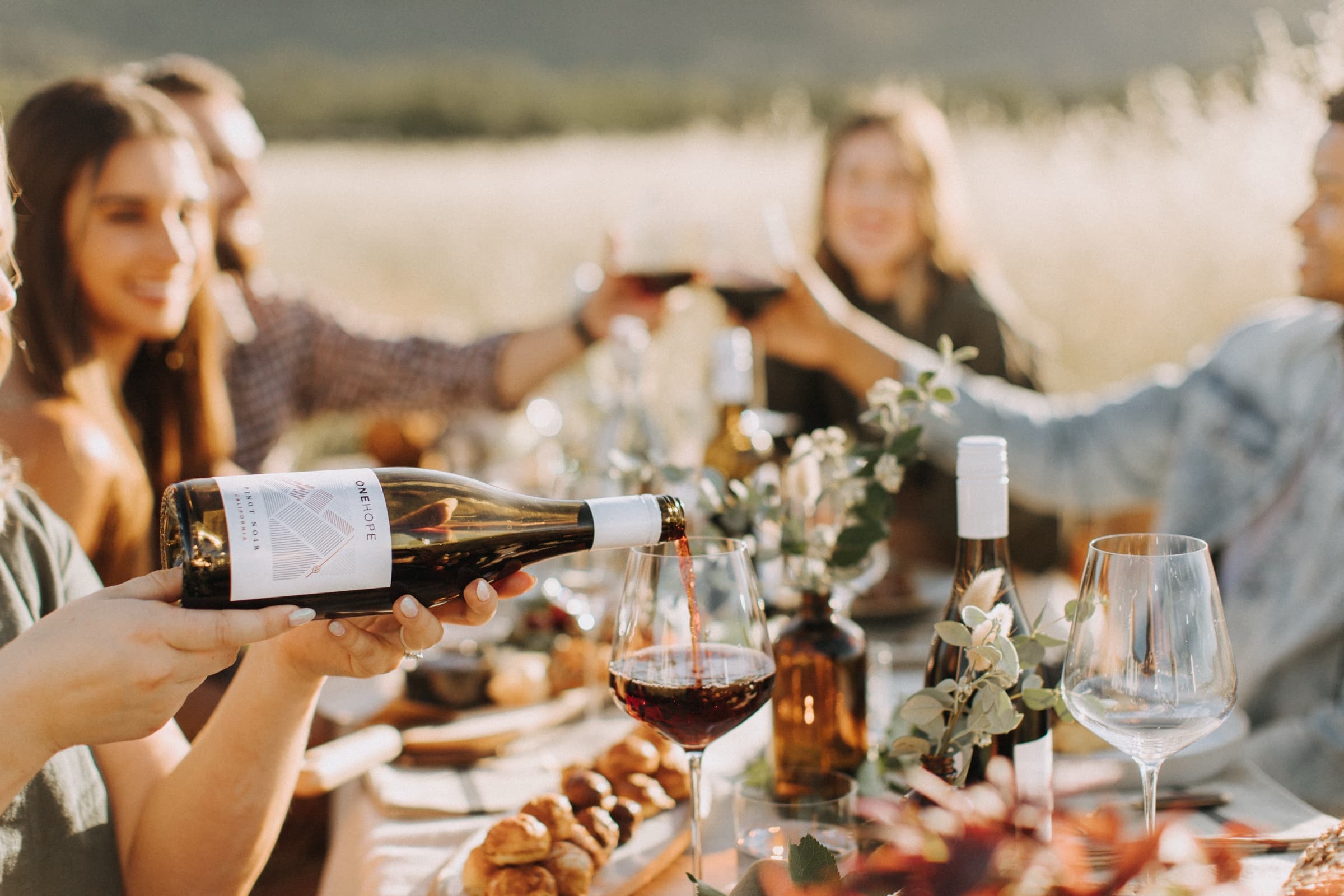 ONEHOPE wine being poured for guests gathered around a vineyard table
